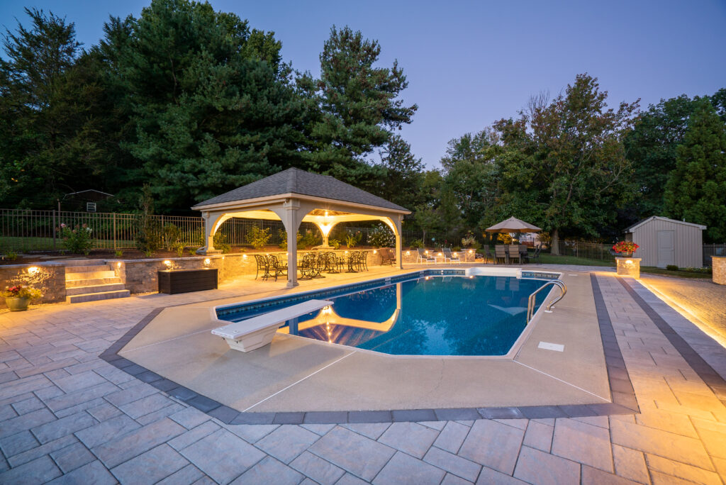An outdoor pool and patio space lit up with different types of lights by Hosler’s Homescapes.