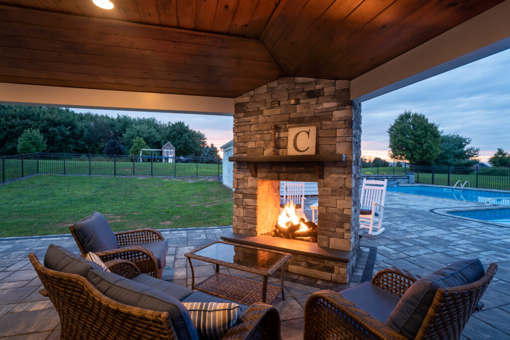 An outdoor fireplace inside a small patio, surrounded by outdoor furniture. Above the mantle is a sign with the letter “C” on it.